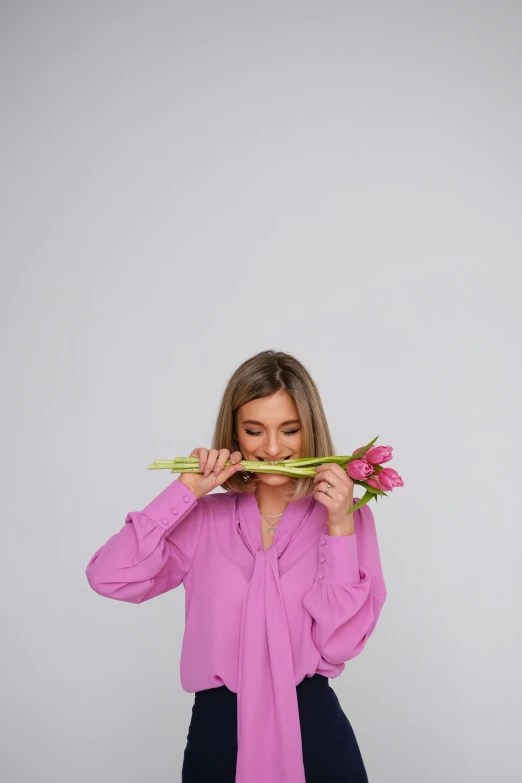 a woman holding flowers in front of her face, pink shirt, bending down slightly, long snout, minimalist photo