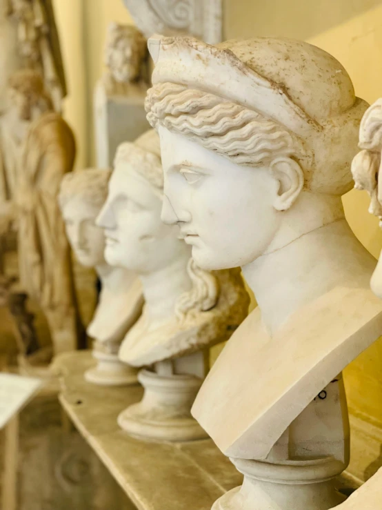 a number of busts on a shelf in a room, a marble sculpture, inspired by Antonio Canova, trending on pexels, made of marble, female, roman city, snapchat photo