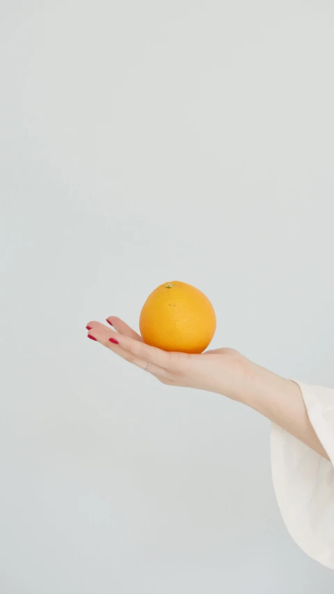 a woman holding an orange in her hand, unsplash, minimalism, square, low quality photo, aoi ogata, small