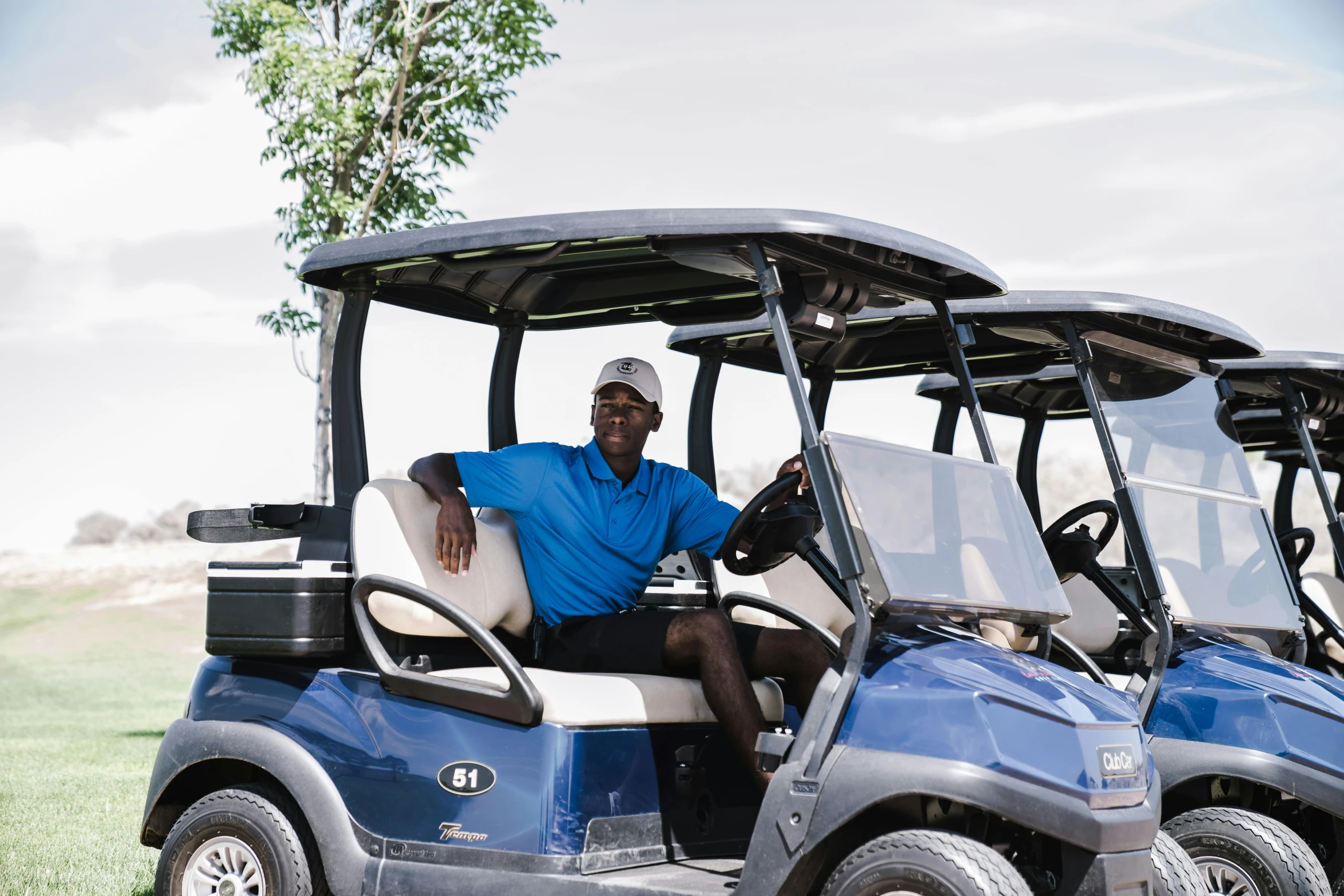 a man sitting in the driver's seat of a blue golf cart, emmanuel shiru, albuquerque, avatar image