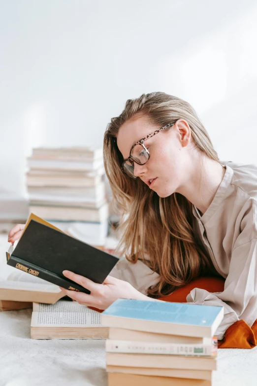 a woman laying on a bed reading a book, trending on pexels, academic art, square rimmed glasses, holding books, gif, 1 2 9 7