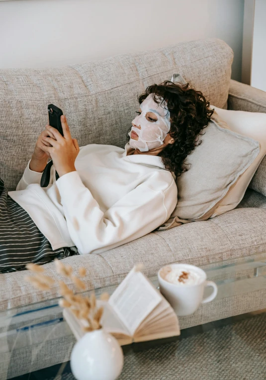 a woman laying on a couch using a cell phone, trending on pexels, happening, wearing a noh theatre mask, skincare, half body photo, seasonal