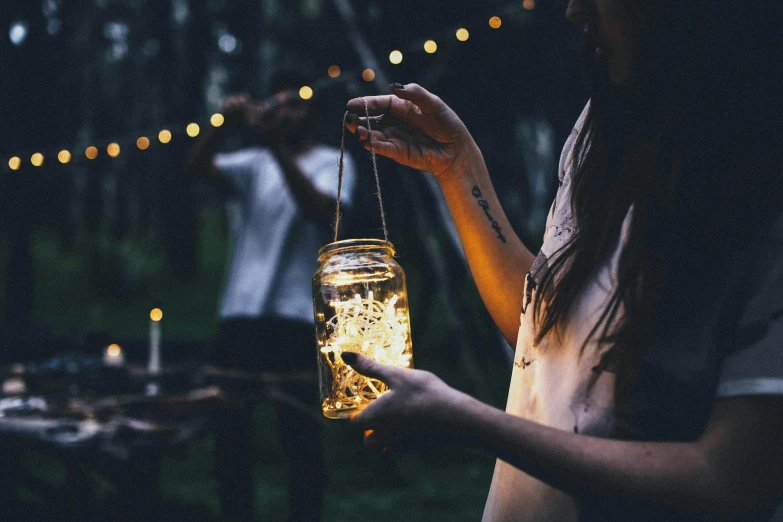 a woman holding a jar filled with fairy lights, by Daniel Lieske, pexels contest winner, al fresco, lantern, instagram post, pale light