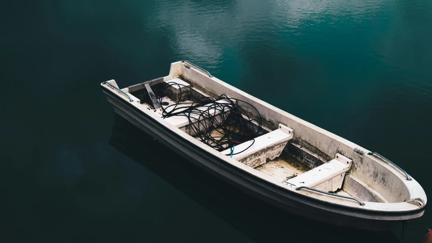 a small white boat floating on top of a body of water, by Elsa Bleda, pexels contest winner, wrecked technology, dark green water, skiff, floating power cables