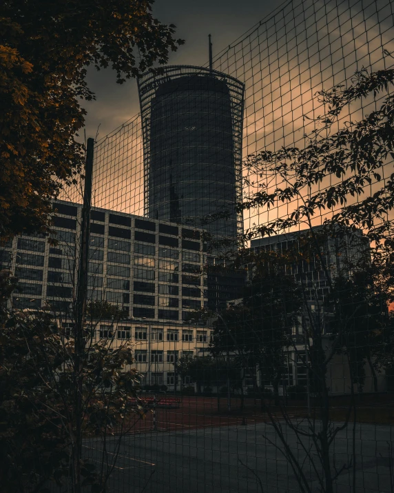 a red fire hydrant sitting in front of a tall building, an album cover, inspired by Elsa Bleda, brutalism, sunset photo, with dark trees in foreground, warsaw, low quality photo