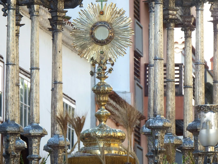 a close up of a clock on a pole in front of a building, a statue, inspired by Francisco Zúñiga, baroque, “ golden chalice, blessing palms, shafts of sunlight in the centre, shiny silver