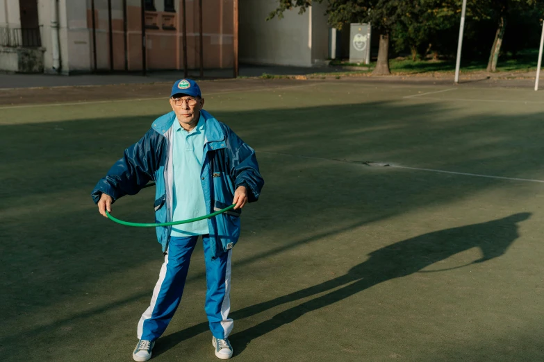 a man standing on a tennis court holding a hula hoop, by Attila Meszlenyi, pexels contest winner, older male, wearing blue jacket, azamat khairov, wearing a track suit