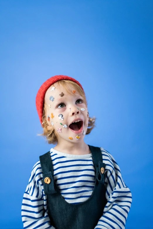 a little boy with food all over his face, an album cover, trending on pexels, visual art, wearing a french beret, colored spots, with a blue background, facepaint facepaint facepaint