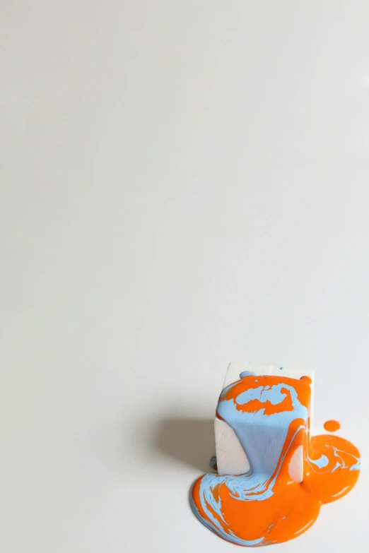 a close up of a toothbrush on a white surface, an abstract sculpture, by Doug Ohlson, conceptual art, orange and blue, cake, cube, paint pour