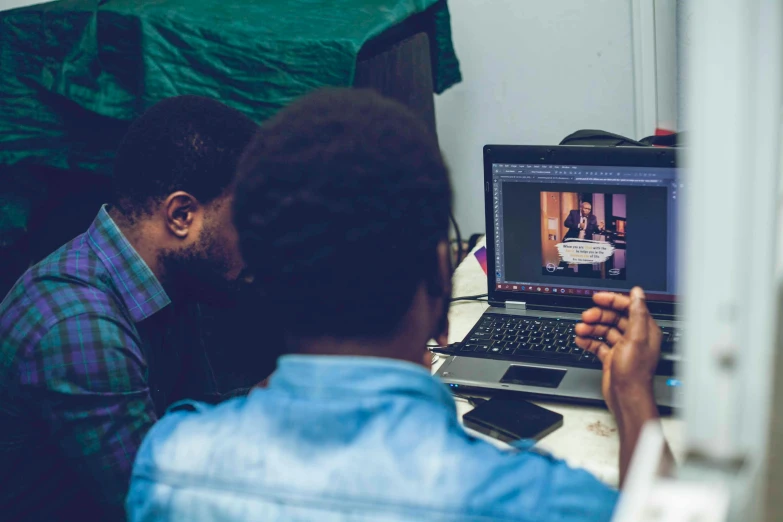 a couple of men sitting in front of a laptop computer, a photo, by Alexander Fedosav, trending on unsplash, in a workshop, afro tech, medium shot taken from behind, instagram photo