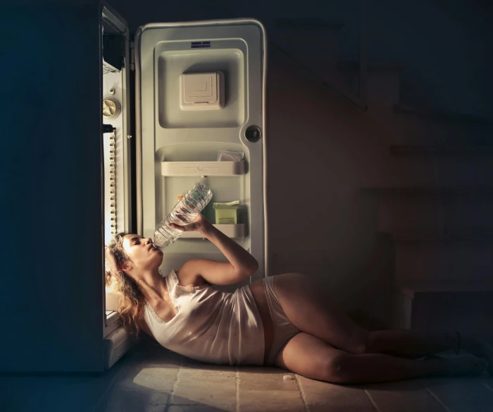 a woman laying on the floor in front of an open refrigerator, inspired by Elsa Bleda, shutterstock contest winner, scary night, full body potrait holding bottle, devouring, summer night