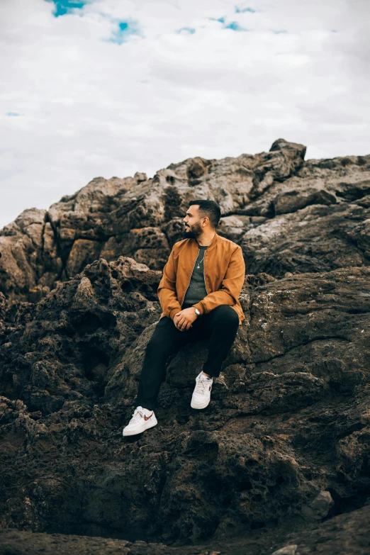 a man sitting on a rock near the ocean, an album cover, pexels contest winner, a portrait of rahul kohli, in australia, сastle on the rock, smart casual