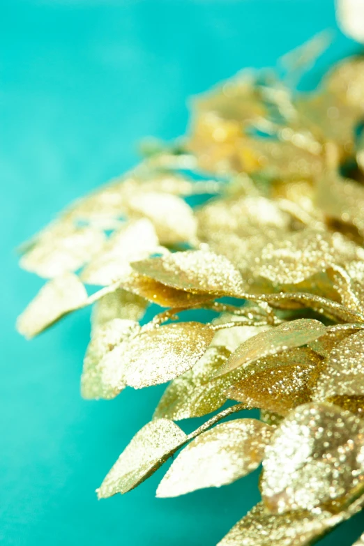 a close up of a gold flower on a blue surface, wearing a laurel wreath, product shot, lianas, glittery