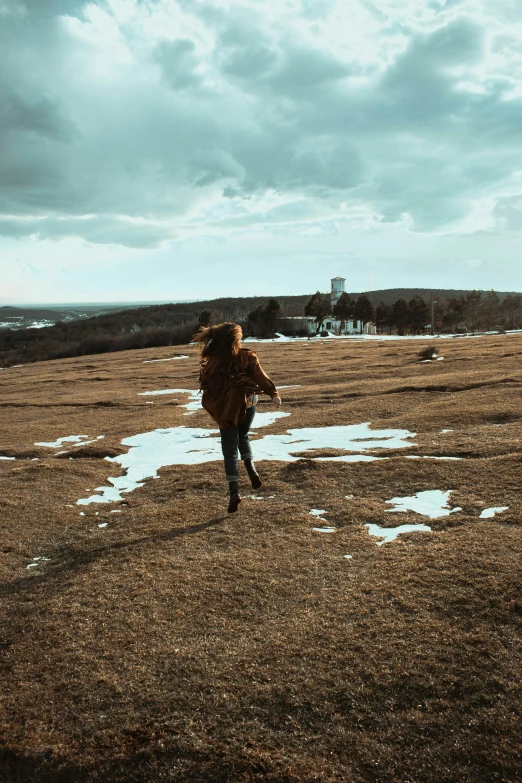 a woman walking across a snow covered field, an album cover, pexels contest winner, grassy hills, william penn state forest, flying shot, brown