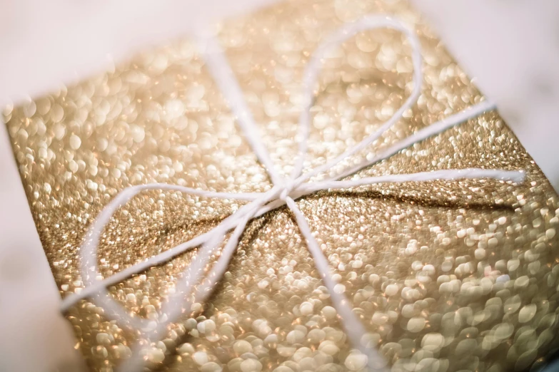 a wrapped gift sitting on top of a table, a stipple, pexels contest winner, renaissance, white and gold color palette, pearlescent skin, closeup, thick bow