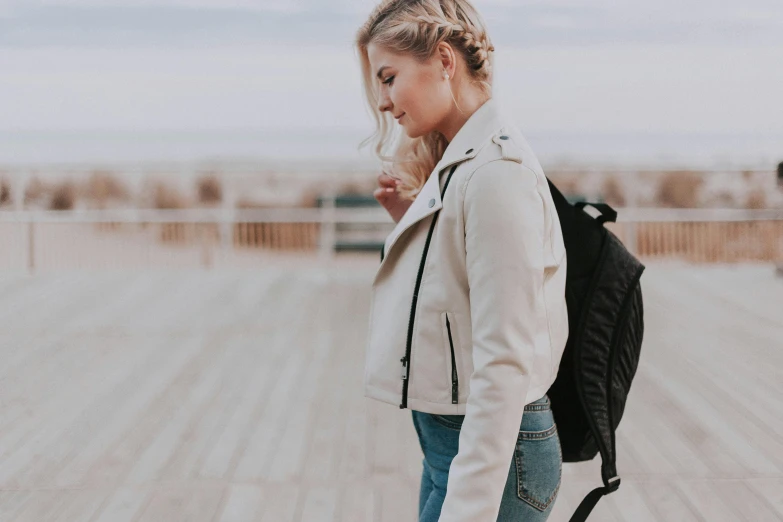 a woman with a backpack walking on a boardwalk, by Christen Købke, trending on pexels, happening, blonde braided hair, leather bomber jacket, outfit : jeans and white vest, profile image
