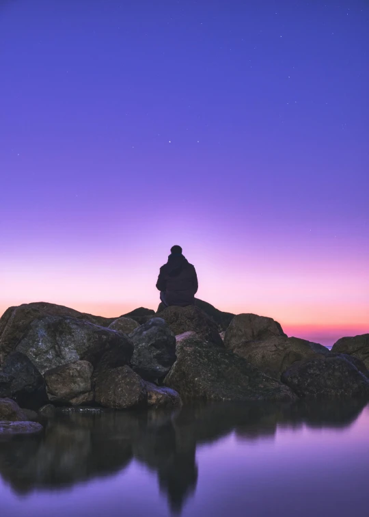 a person sitting on top of a rock next to a body of water, unsplash, romanticism, purple omnious sky, meditation, full frame image, sittin