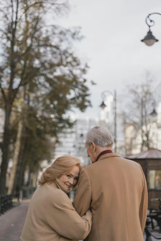 a man and a woman standing next to each other, a photo, unsplash, visual art, white haired lady, in a city square, brown, february)