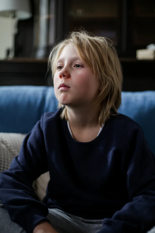 a young boy sitting on top of a blue couch, inspired by William John Thomson, pexels, looking away from camera, window light, television still, a blond