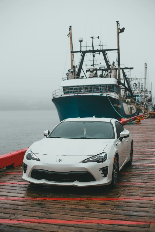 a white sports car parked on a dock next to a boat, by Carey Morris, pexels contest winner, renaissance, frontal pose, low fog, toyota supra, port scene background