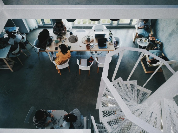 a group of people sitting around a table in a room, spiral stairs, open office, flatlay, leaking