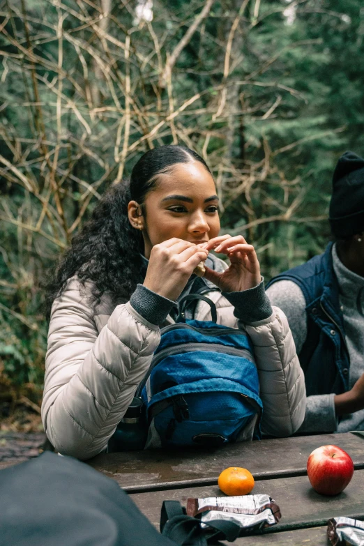 a group of people sitting around a picnic table, a portrait, trending on pexels, model wears a puffer jacket, having a snack, trekking in a forest, tessa thompson