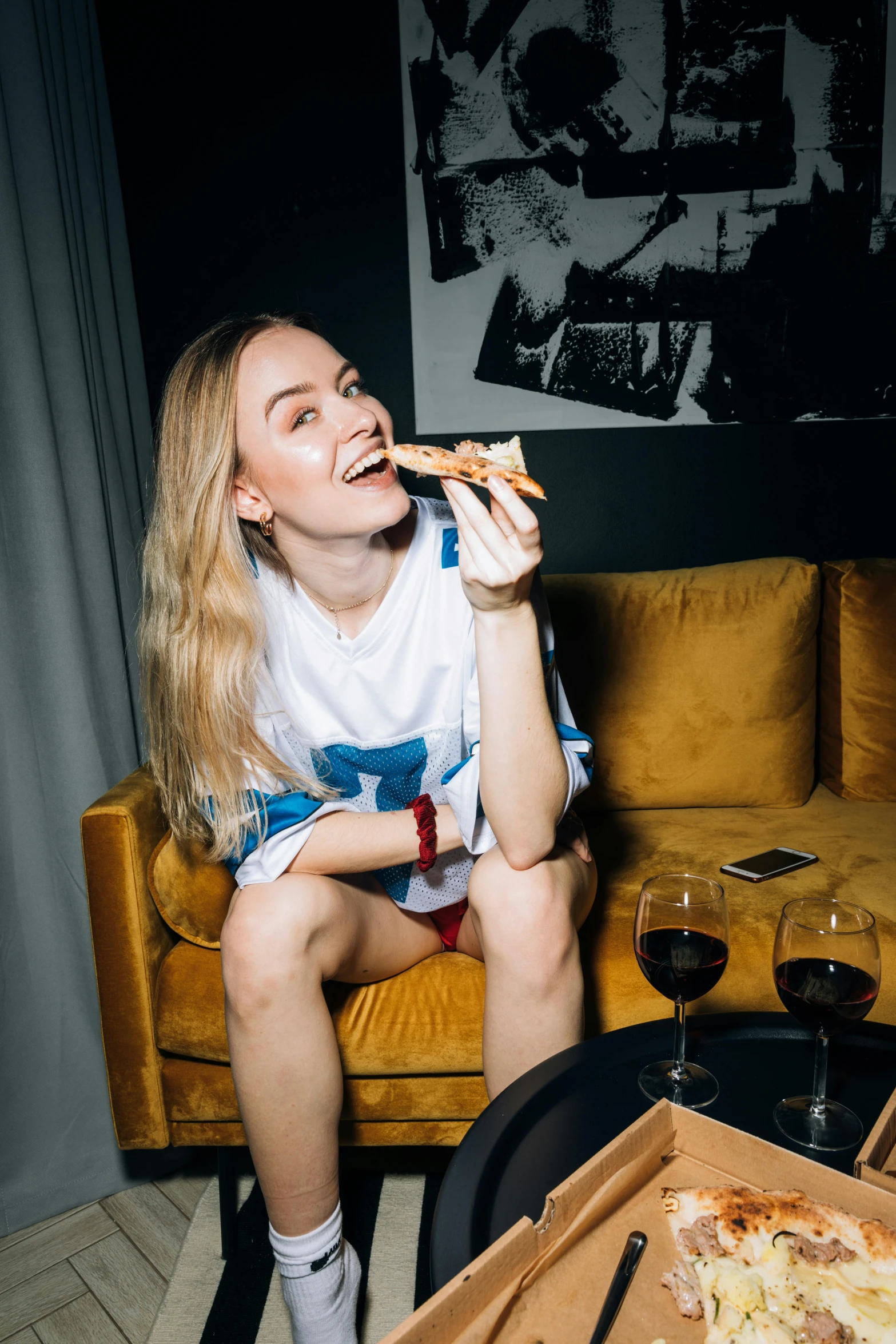 a woman sitting on a couch eating a slice of pizza, by Sara Saftleven, pexels contest winner, happening, sophie turner girl, wearing pants and a t-shirt, kirsi salonen, 🍸🍋