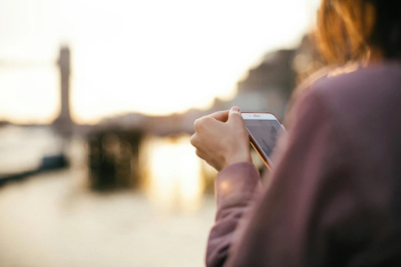 a close up of a person holding a cell phone, a picture, gazing at the water, warm coloured, late afternoon, surrounding the city