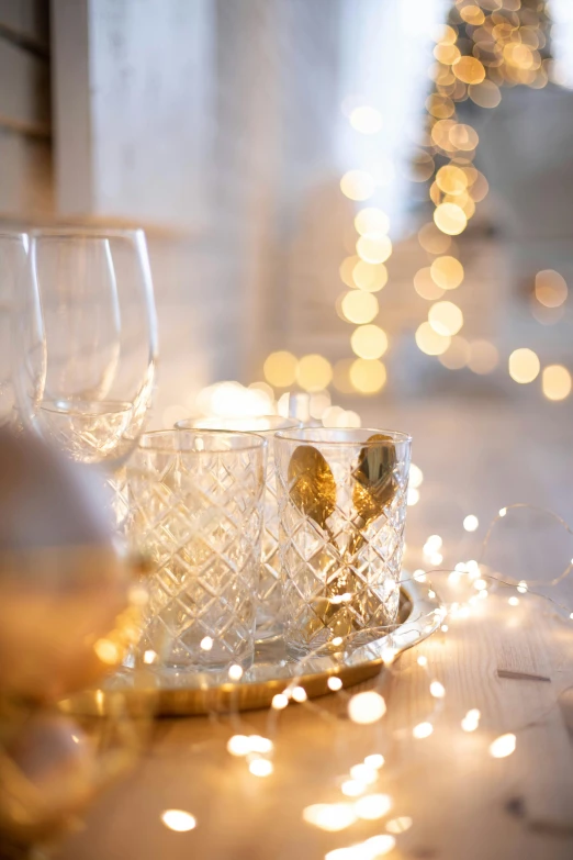 a couple of wine glasses sitting on top of a table, light and space, gold decorations, warmly lit, light scatter, bubbly