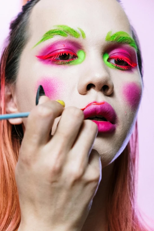 a woman is putting makeup on her face, an album cover, by Julia Pishtar, colourful close up shot, dayglo pink, pose 4 of 1 6, making of