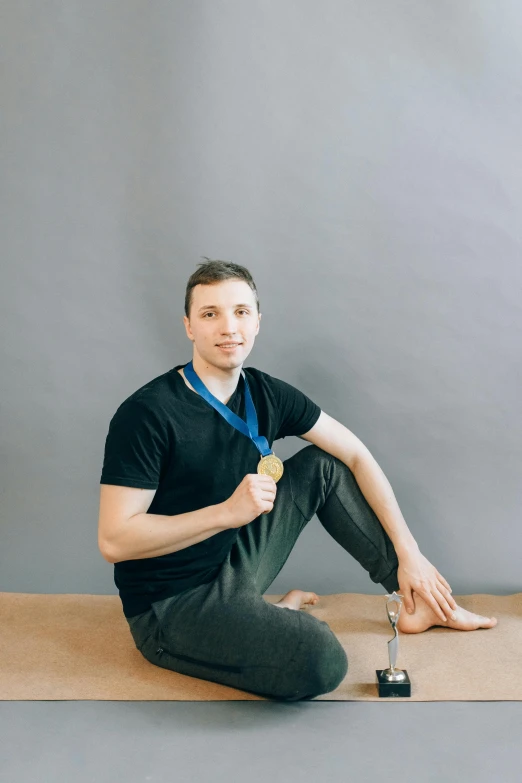 a man sitting on a yoga mat with a medal around his neck, a picture, by Adam Marczyński, young adult male, professional profile picture, dasha taran, young man with medium - length