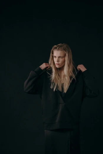 a woman standing in front of a black background, inspired by Louisa Matthíasdóttir, unsplash, minimalism, wearing a black hoodie, erin moriarty, julian ope, set against a white background