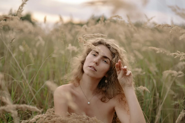 a woman sitting in a field of tall grass, inspired by Elsa Bleda, trending on pexels, magic realism, wearing nothing, wavy hair spread out, portrait image, androgynous person