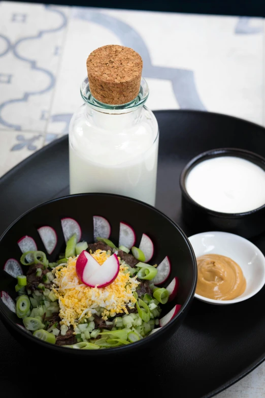 a black plate topped with a salad next to a bottle of milk, mayan, yogurt, curated collection, hispanic