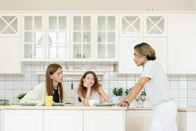 a woman serving food to two women in a kitchen, by Emma Andijewska, pexels, arguing, white, minimal kitchen, husband wife and son