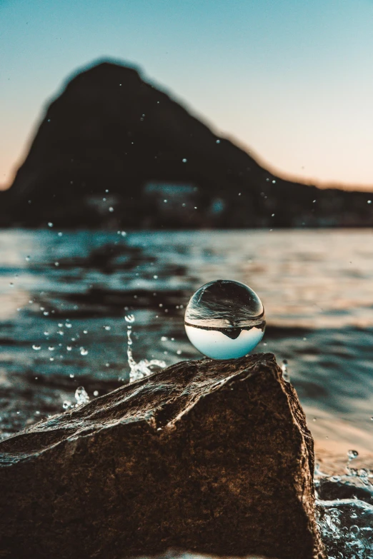 a glass ball sitting on top of a rock in the water, gazing at the water, water dripping, water type, skewed shot
