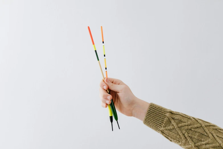 a person holding two colored pencils in their hand, a minimalist painting, inspired by Alexander Calder, unsplash, kinetic art, magical fishing rod weapon, high quality product photo, skewer, tactile buttons and lights