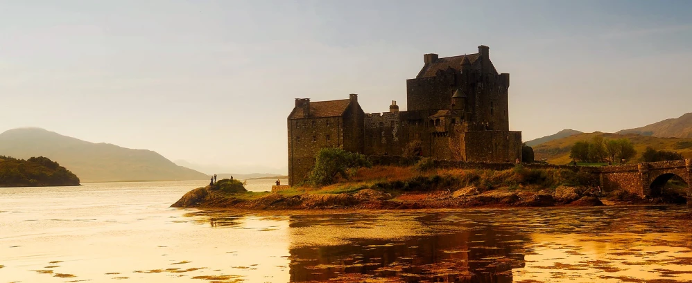 a castle sitting on top of a hill next to a body of water, inspired by Dugald Sutherland MacColl, pexels contest winner, dramatic warm morning light, panoramic, october, fan favorite