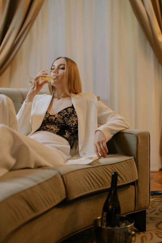 a woman sitting on a couch drinking a glass of wine, by Adam Marczyński, trending on pexels, renaissance, white suit and black tie, sitting on the bed, haute couture fashion shoot, drinking whiskey