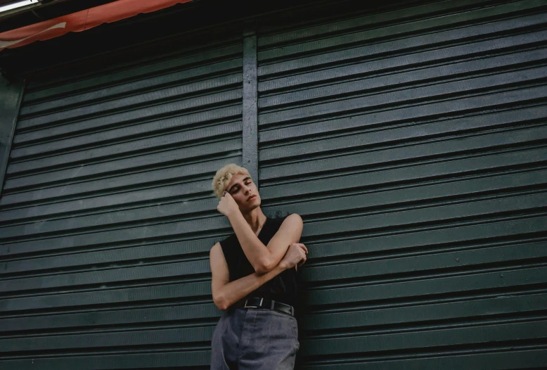 a man leaning against a garage door talking on a cell phone, an album cover, inspired by Elsa Bleda, pexels contest winner, realism, short platinum hair tomboy, beautiful androgynous girl, silo, non binary model