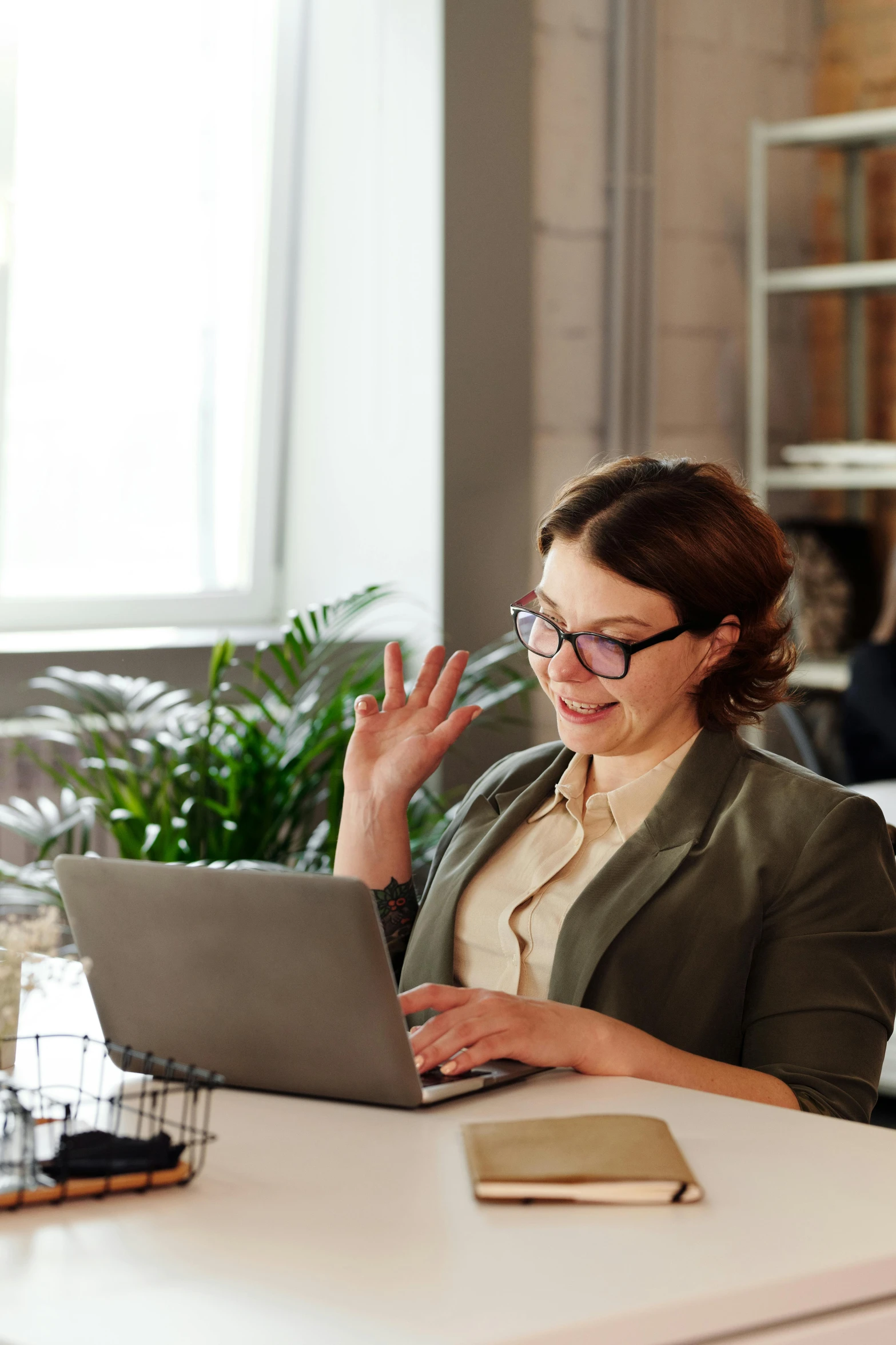 a woman sitting at a table with a laptop, waving, curated collections, professional grade, thumbnail