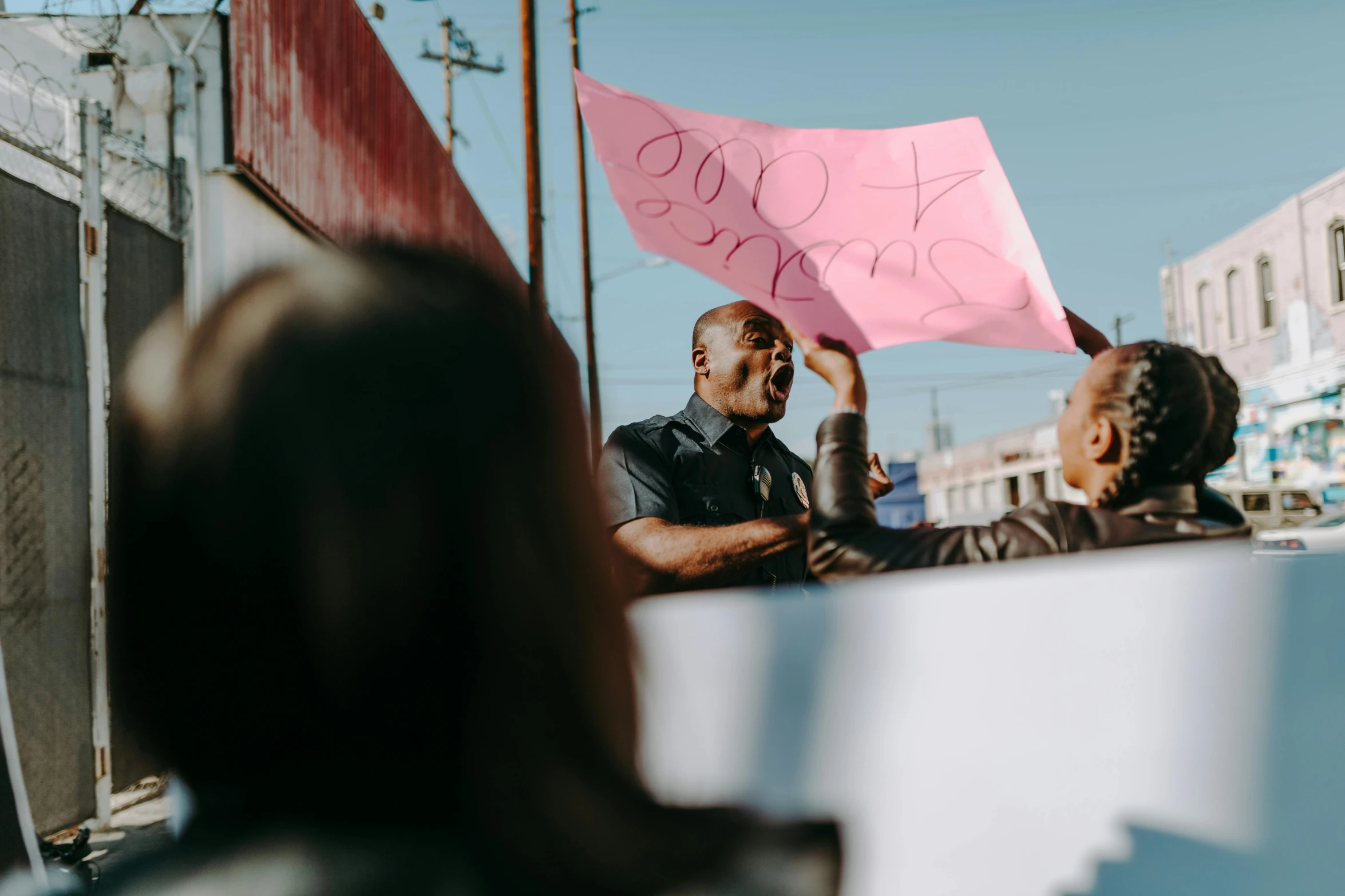 a man standing next to a woman holding a pink sign, a photo, trending on pexels, excessivism, panel of black, protest, looking across the shoulder, los angeles ca
