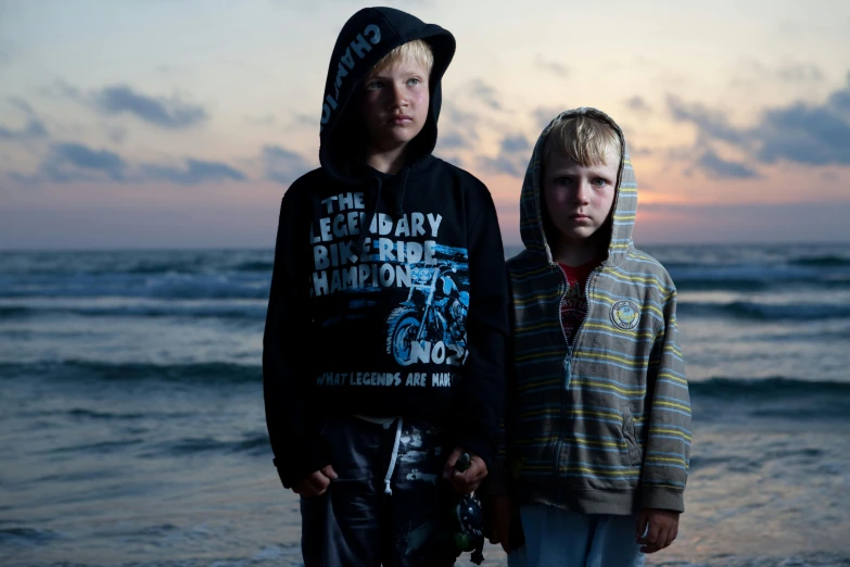 a couple of young boys standing on top of a beach, an album cover, unsplash, hyperrealism, ominous evening, serious faces, ukraine. photography, taken in the late 2010s