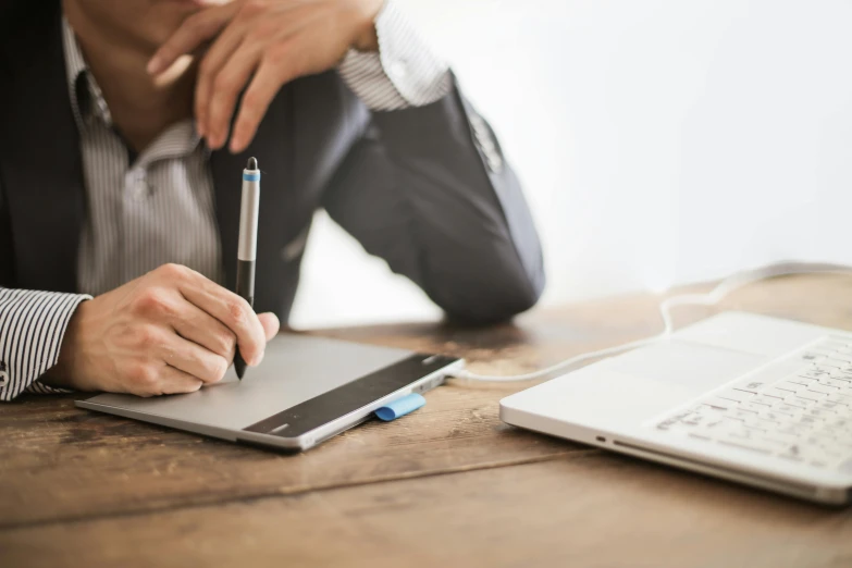 a person sitting at a table with a laptop and a pen, 9 9 designs, writing on a clipboard, thumbnail, professional lightimg