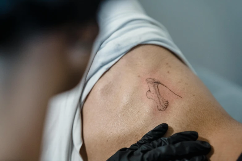 a person with a tattoo on their arm, a tattoo, by Adam Marczyński, trending on pexels, hyperrealism, holding a magic needle, faded outline, over-shoulder shot, cysts