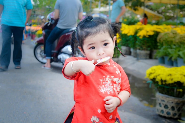 a little girl in a red dress brushing her teeth, a picture, inspired by Cui Bai, pexels contest winner, with street food stalls, avatar image, square, cute pout