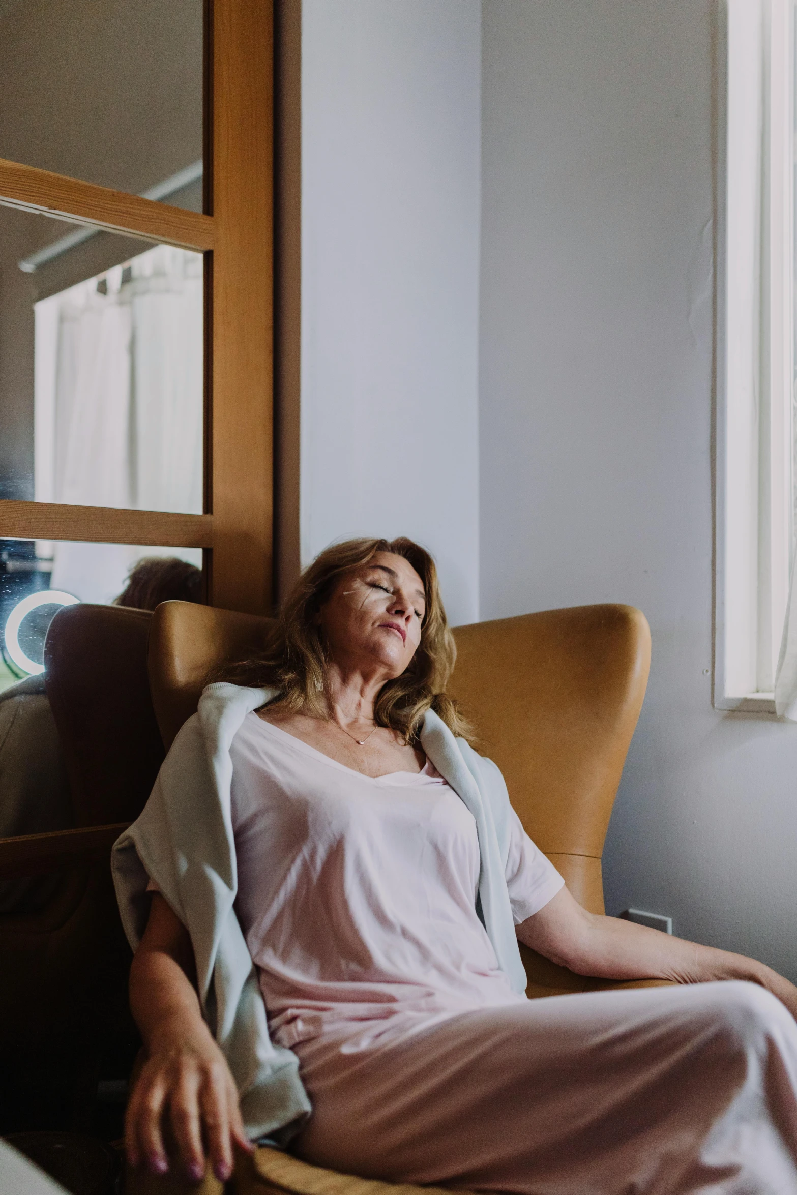 a woman sitting in a chair next to a window, eyes closed, calming, in sao paulo, hotel room