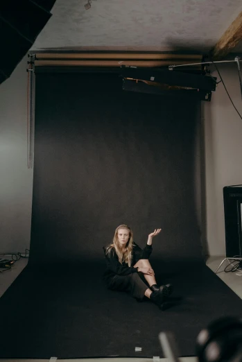 a woman sitting on the ground in front of a black backdrop, unsplash, inside a grand studio, britt marling style 3/4, holding it out to the camera, journalism photo