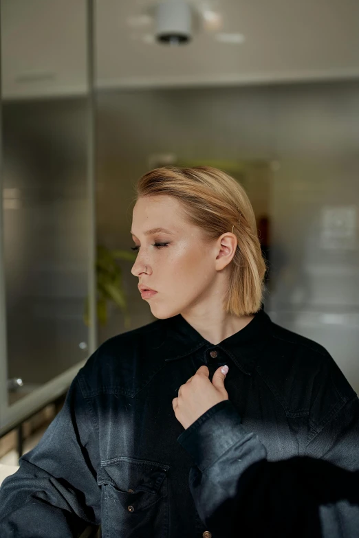 a woman standing in a kitchen preparing food, an album cover, inspired by Sigrid Hjertén, unsplash, realism, black jacket | shiny, looking from side, a blond, profile portrait