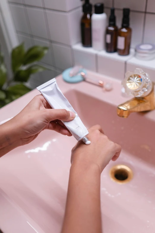 a woman brushing her teeth in front of a pink sink, inspired by Elsa Bleda, detailed product image, back of hand on the table, tubes, smooth bioluminescent skin